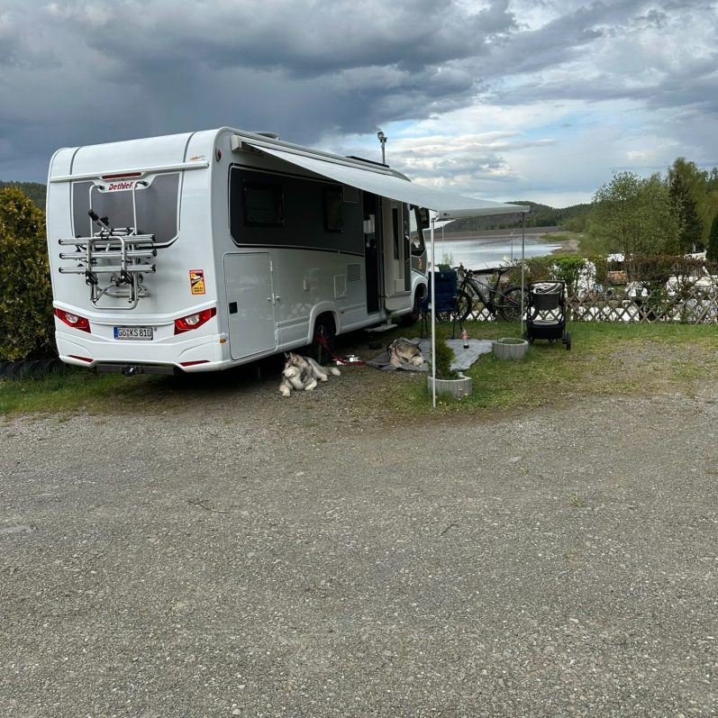 Wohnmobilparkplatz am Ufer mit ruhiger Landschaft und bewölktem Himmel.